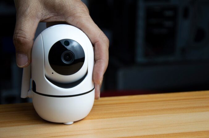 Main tenant une petite caméra de surveillance intérieure blanche et noire sur une table en bois