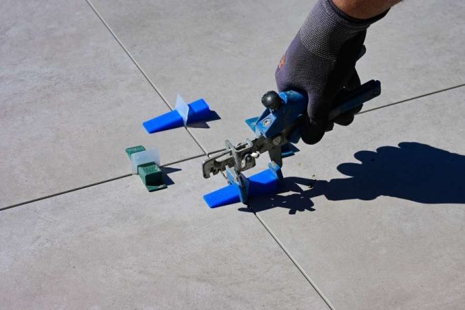 Un artisan utilise une pince pour aligner des carreaux, une étape cruciale avant de choisir la couleur des joints de carrelage.