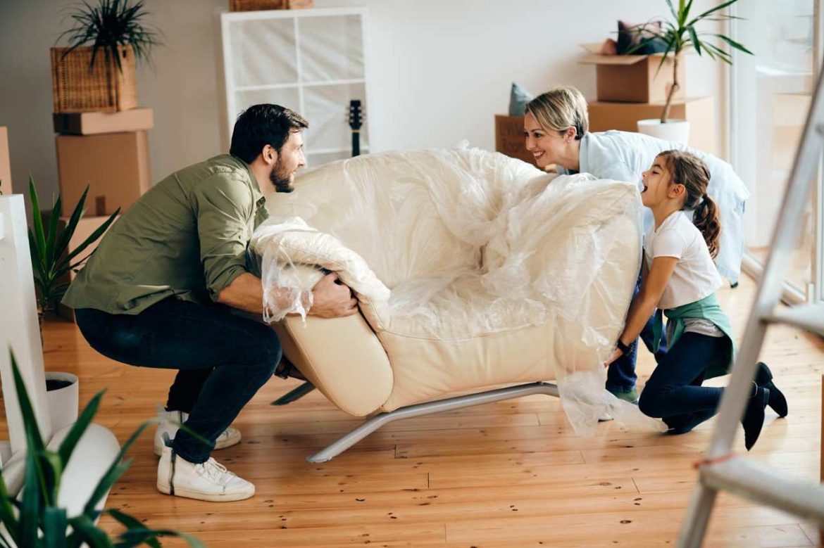 Une famille déballe et déplace un canapé au milieu des cartons pour concrétiser leurs idées aménagement salon moderne après un emménagement.