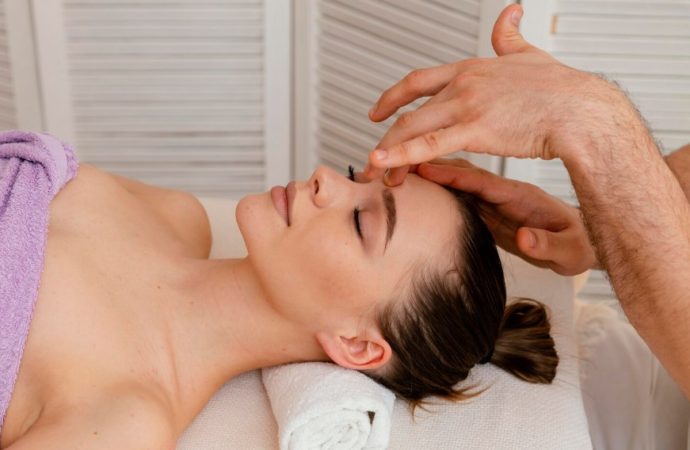 Massothérapeute pratiquant un massage régulier du visage et du front sur une femme allongée aux yeux fermés.