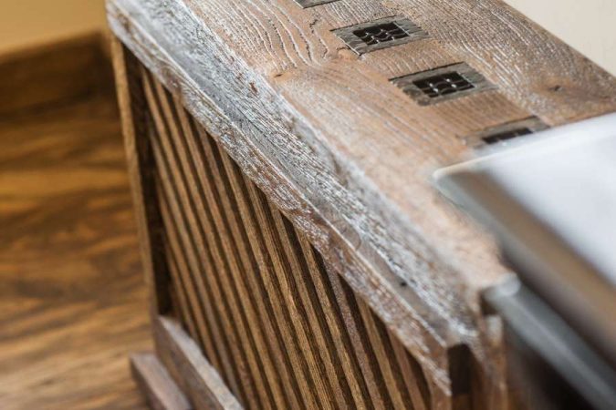 Un cache-radiateur en bois rustique avec une façade en lattes diagonales et des grilles d'aération sur le plateau supérieur.
